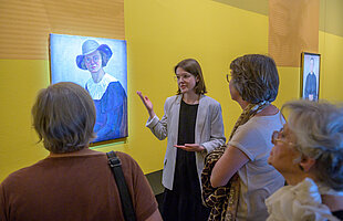 Besucher*innen beim Rundgang mit der Kuratorin durch die Ausstellung „Bildgeschichten“, sie stehen vor einem Frauenporträt, Foto: Daniel Schvarcz / Jüdisches Museum München 