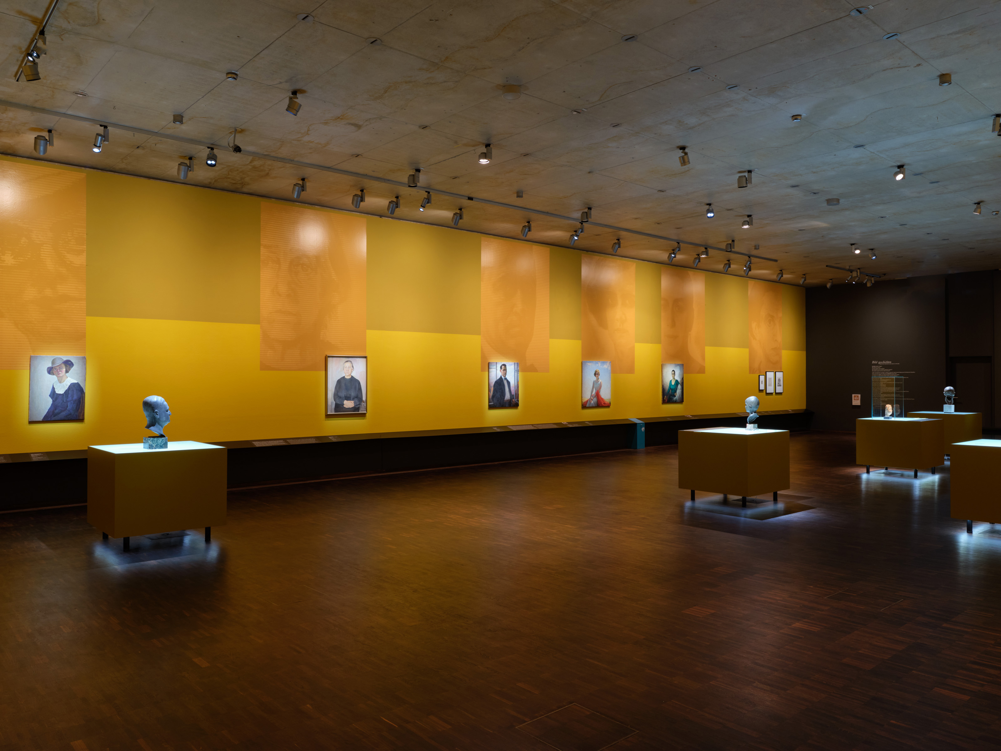 Exhibition view "Picture Stories. Portraits of Munich Jews" - several portraits hang side by side in an exhibition room in shades of yellow, large blow-ups reflect the motif of the portraits, photo: Eva Jünger / Jewish Museum Munich 