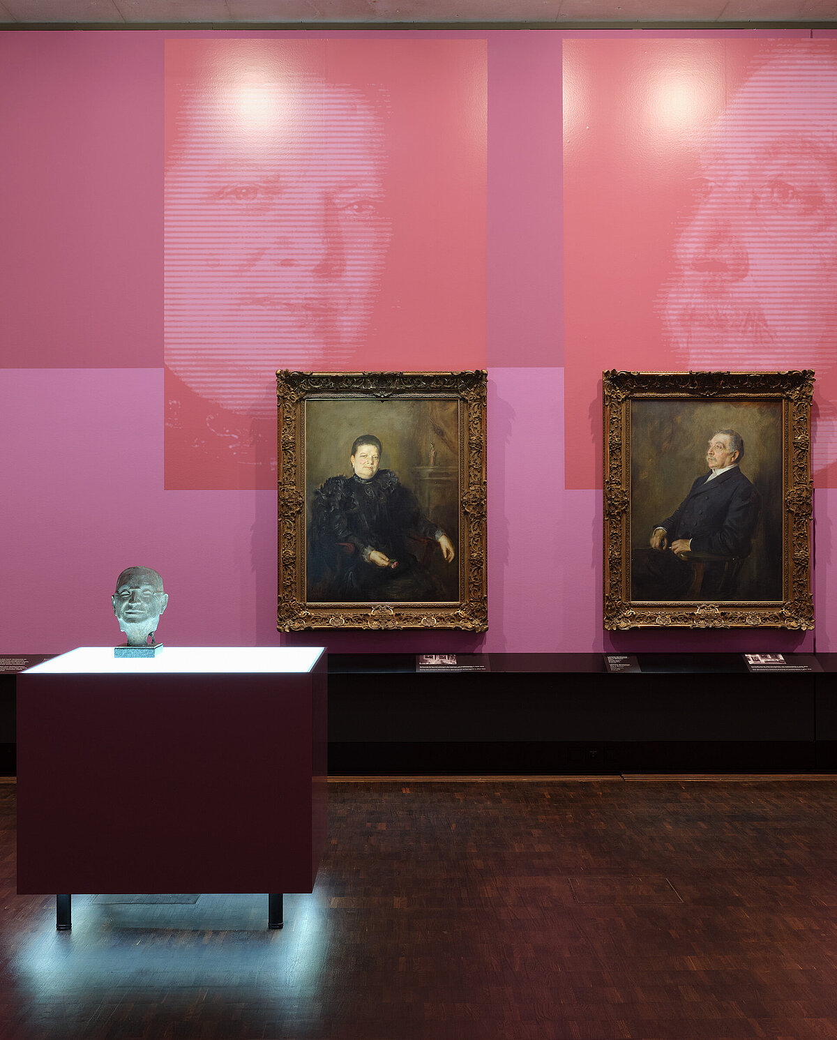 Exhibition view "Picture Stories", portraits of Fanny and Lehmann Bernheimer hanging on a rose-colored wall, in front of them the bust of Otto Bernheimer on an illuminated display case, Photo: Eva Jünger / Jewish Museum Munich